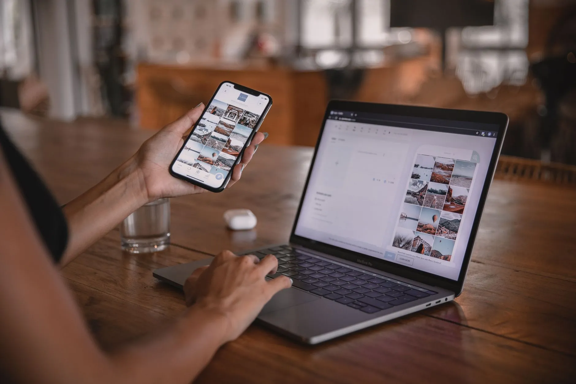 Девушка в кафе редактирует пост для соцсетей на смартфоне, рядом открыт ноутбук